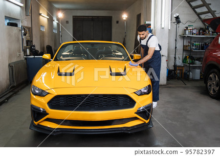 Wash worker man, wearing protective clothes uniform overalls , cleaning modern yellow luxury car Wash worker man, wearing protective clothes uniform overalls , cleaning modern yellow luxury car 95782397
