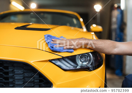 Close up of hand of male car wash worker holds the microfiber in hand and polishes car hood Close up of hand of male car wash worker holds the microfiber in hand and polishes car hood 95782399