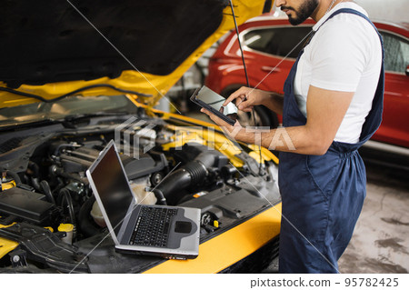 Cropped view of mechanic using tablet computer, recording automobile engine checks Cropped view of mechanic using tablet computer, recording automobile engine checks 95782425