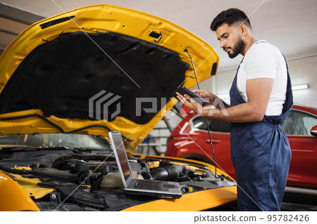Serious focused man car technician mechanic repairing car problem of engine, during system checking 95782426