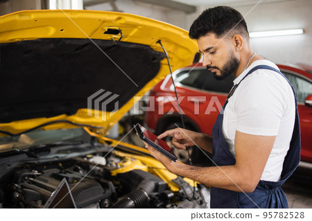 Serious focused man car technician mechanic repairing car problem of engine, during system checking Serious focused man car technician mechanic repairing car problem of engine, during system checking 95782528