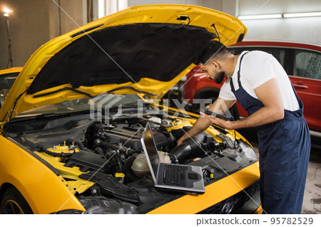 Young mechanic using tablet recording automobile engine checks collect detailed information 95782529