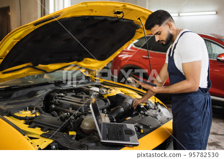 Young mechanic using tablet recording automobile engine checks collect detailed information 95782530