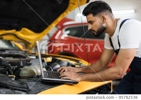 Car mechanic maintains vehicle using diagnostic laptop computer for checking engine problems Car mechanic maintains vehicle using diagnostic laptop computer for checking engine problems 95782536