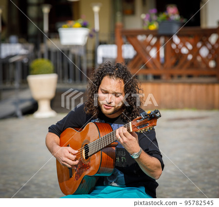 A street musician plays the guitar, entertains people in the city square. 95782545