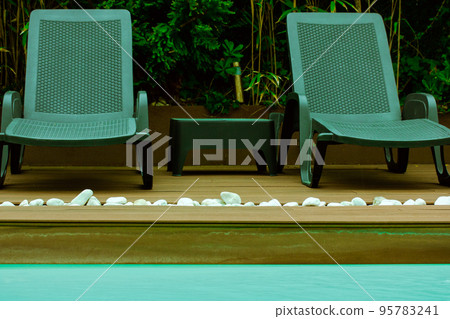 Black deck chairs, garden furniture for relaxing by a swimming pool with blue water. Relaxation area, lounge zone at a luxury summer resort, hotel, villa without people. Travel for vacations abroad. Black deck chairs, garden furniture for relaxing by a swimming pool with blue water. Relaxation area, lounge zone at a luxury summer resort, hotel, villa without people. Travel for vacations abroad. 95783241
