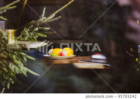 Cozy home atmosphere. View of the interior of room or kitchen inside the outside of a house in a pine forest. Pine tree branch in the foreground. Plate with fruits on a table. Sweet home. Forest house Cozy home atmosphere. View of the interior of room or kitchen inside the outside of a house in a pine forest. Pine tree branch in the foreground. Plate with fruits on a table. Sweet home. Forest house 95783242