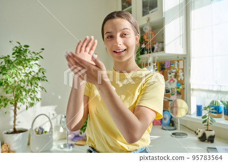 Teenage girl looking at camera clapping her hands, in room 95783564