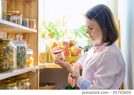 Young woman in kitchen with containers jars of food, holding jar of spices ground red pepper 95783609