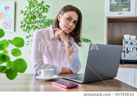 Young woman working at home using laptop, looking at camera 95783610