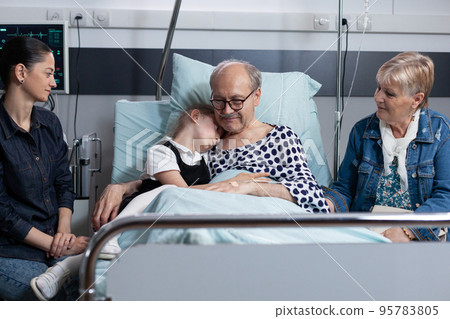 Little girl hugging grandfather at sanatorium room before surgery in medical tower. Hospitalized old man saying goodbye to close family members at elderly people hospital. 95783805