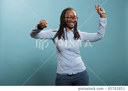 Beautiful attractive young lady dancing and vibing to funky disco music playlist on blue background. Happy energetic adult woman having fun with dance while enjoying melody. Studio shot 95783851