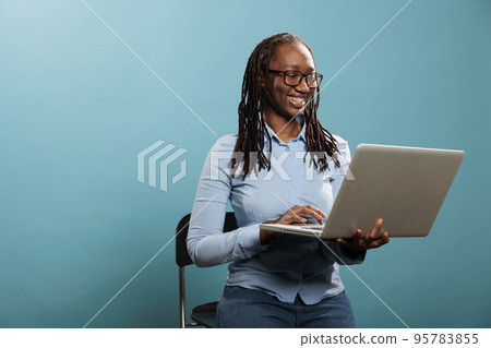 Joyful pretty woman with portable modern computer standing on blue background while surfing web. Excited happy woman having laptop and smiling heartily while browsing webpages on internet 95783855
