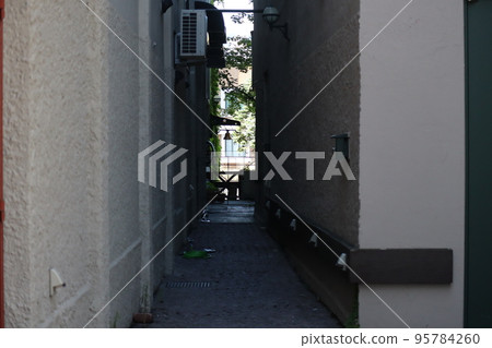 建築物之間的小巷風景和前方可以看到的樹木和建築物的城市景觀 95784260