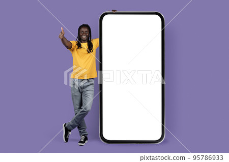 Happy black guy posing with huge smartphone, showing thumb up 95786933