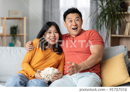 Loving asian couple watching comedy movie together at home Loving asian couple watching comedy movie together at home 95787038