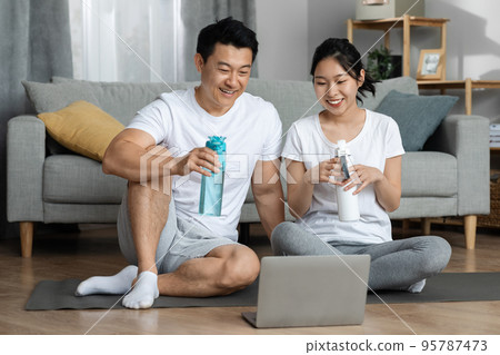 Cheerful chinese man and woman drinking water after workout Cheerful chinese man and woman drinking water after workout 95787473