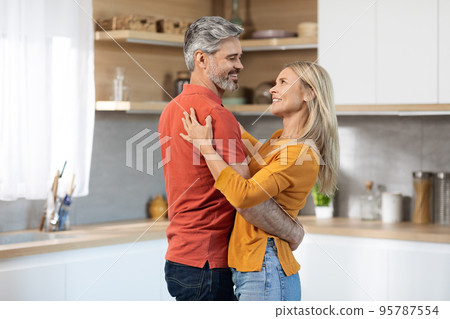 Happily married middle aged couple dancing at kitchen 95787554