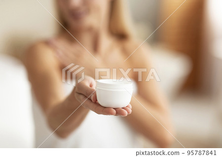 Caucasian woman holding jar of body cream, applying skin care product after shower at home, selective focus, closeup 95787841