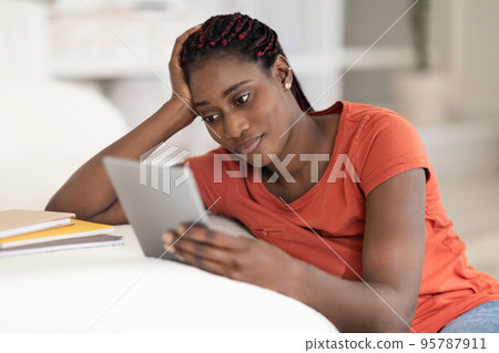 Young Black Woman Using Digital Tablet While Sitting At Desk At Home Young Black Woman Using Digital Tablet While Sitting At Desk At Home 95787911