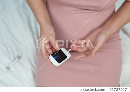 pregnant woman holding glucose meter and checking blood sugar level by herself at home. gestational diabetes concept. pregnant woman holding glucose meter and checking blood sugar level by herself at home. gestational diabetes concept. 95787927