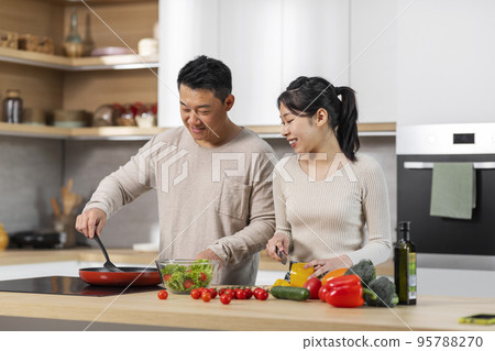 Beautiful asian couple chatting while cooking dinner together 95788270