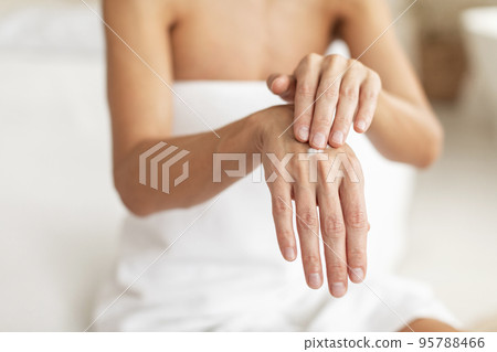 Closeup shot of middle aged woman applying drop of moisturising cream on hands, using nourishing lotion for dry skin 95788466