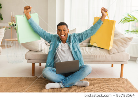 Laughing excited millennial african american male with laptop and many bags rejoices to huge sale 95788564