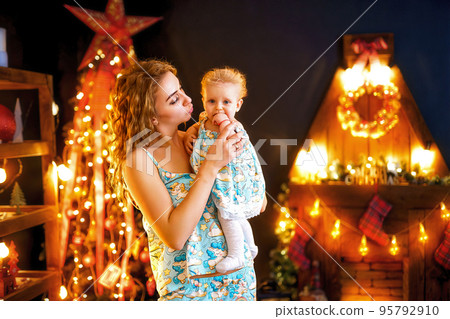 Mother with her baby standing near Christmas tree and fireplace in living room. New Year concept Mother with her baby standing near Christmas tree and fireplace in living room. New Year concept 95792910