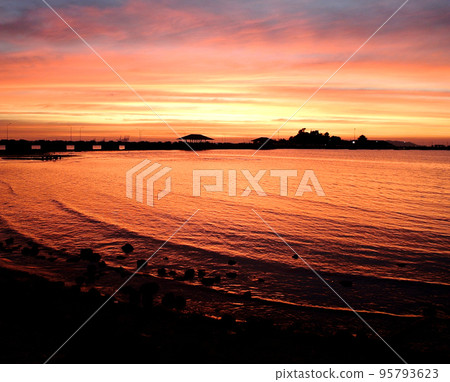 Dramatic sky and reflection at sea surface with silhouette of bridge and island Dramatic sky and reflection at sea surface with silhouette of bridge and island 95793623
