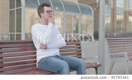 Pensive Young Man Thinking while Sitting Outdoor on Bench 95795361