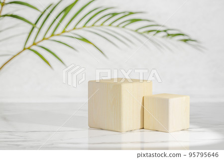 Wooden podiums with green palm leaf in sunlight on white marble table and gray wall. Fashion showcase for cosmetic products, goods. Minimal product display 95795646