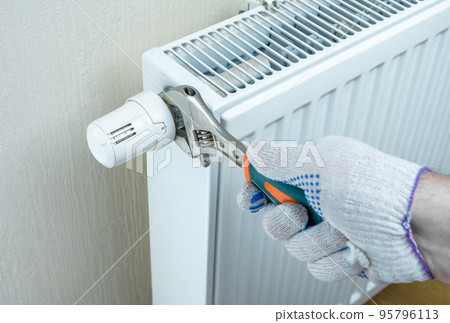 saving energy resources. hand with an adjustable wrench regulates heat on heating radiator in order to save. energy efficiency at home saving energy resources. hand with an adjustable wrench regulates heat on heating radiator in order to save. energy efficiency at home 95796113