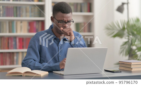 Young African Man Coughing while using Laptop in Office 95796170