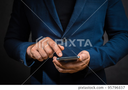 businessman in suit manages business processes using mobile phone on dark background. man touching screen modern smartphone. 95796837