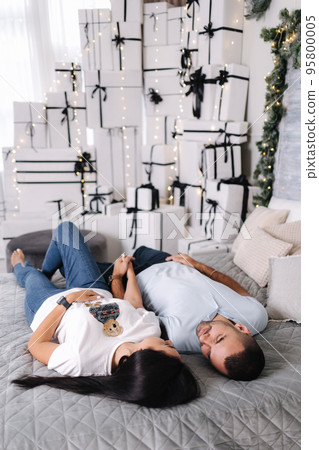 Cute couple lie on the bad in front of big pile of gifts. Christmas time Cute couple lie on the bad in front of big pile of gifts. Christmas time 95800005