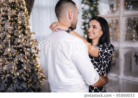 Handsome man with his beautiful woman hug each other at home at Christmas eve. Fit tree and snow outsif. Christmas mood Handsome man with his beautiful woman hug each other at home at Christmas eve. Fit tree and snow outsif. Christmas mood 95800033