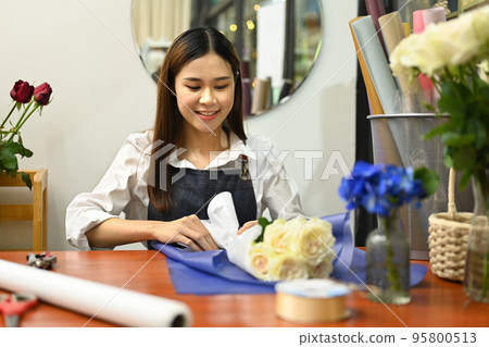 Smiling young female florist wearing apron making bouquet, decorations and arrangements flower studio 95800513