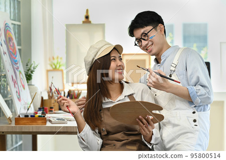 Smiling handsome male artist and his girlfriend painting together at bright cozy art studio Smiling handsome male artist and his girlfriend painting together at bright cozy art studio 95800514