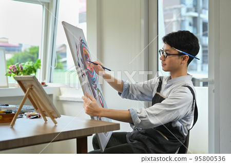 Pleasant man painting picture with watercolor at cozy home studio. Art, creative hobby and leisure activity concept Pleasant man painting picture with watercolor at cozy home studio. Art, creative hobby and leisure activity concept 95800536
