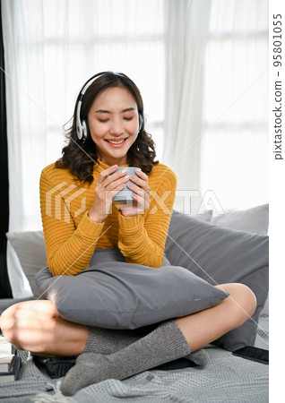 Relaxed Asian woman wearing headphones, listening to music and enjoying coffee Relaxed Asian woman wearing headphones, listening to music and enjoying coffee 95801055