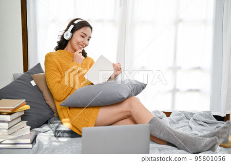 Attractive Asian woman listening to music while reading a book in her living room. 95801056