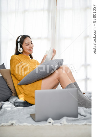 Gorgeous Asian woman listening to music and reading a book while relaxing sitting by the window Gorgeous Asian woman listening to music and reading a book while relaxing sitting by the window 95801057