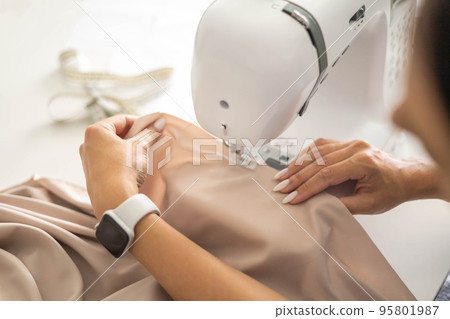 Woman tailor dressmaker hands fabric clothes manufacture workshop on sewing machine closeup Woman tailor dressmaker hands fabric clothes manufacture workshop on sewing machine closeup 95801987