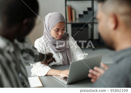 Young Muslim female student networking while two men pointing at her Young Muslim female student networking while two men pointing at her 95802109
