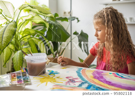 Laughing blonde curly little girl drawing paper art picture chalks sitting on near childish hovel Laughing blonde curly little girl drawing paper art picture chalks sitting on near childish hovel 95802118