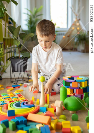 Confident male kid building fortress tower architecture and forest with trees wooden bricks ecology Montessori material Confident male kid building fortress tower architecture and forest with trees wooden bricks ecology Montessori material 95802182