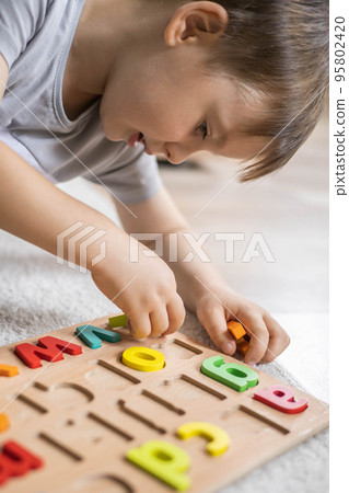 Male kid playing with wooden eco friendly alphabet letters board on table top view intellectual game Male kid playing with wooden eco friendly alphabet letters board on table top view intellectual game 95802420