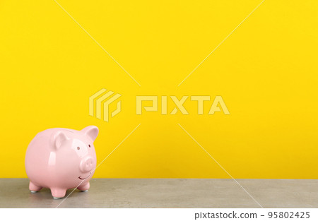 Pink piggy bank on light grey table against yellow background. Space for text 95802425