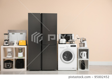 Modern refrigerator and other household appliances near beige wall indoors 95802452